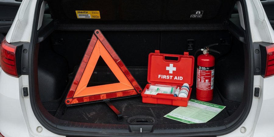 Open kofferbak van huurauto met driehoek, EHBO-kit en brandblusser